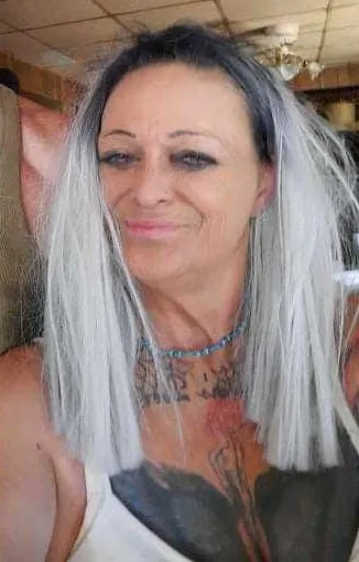 Linda Dillard with long silver hair, a beaded necklace and tattoos on her chest